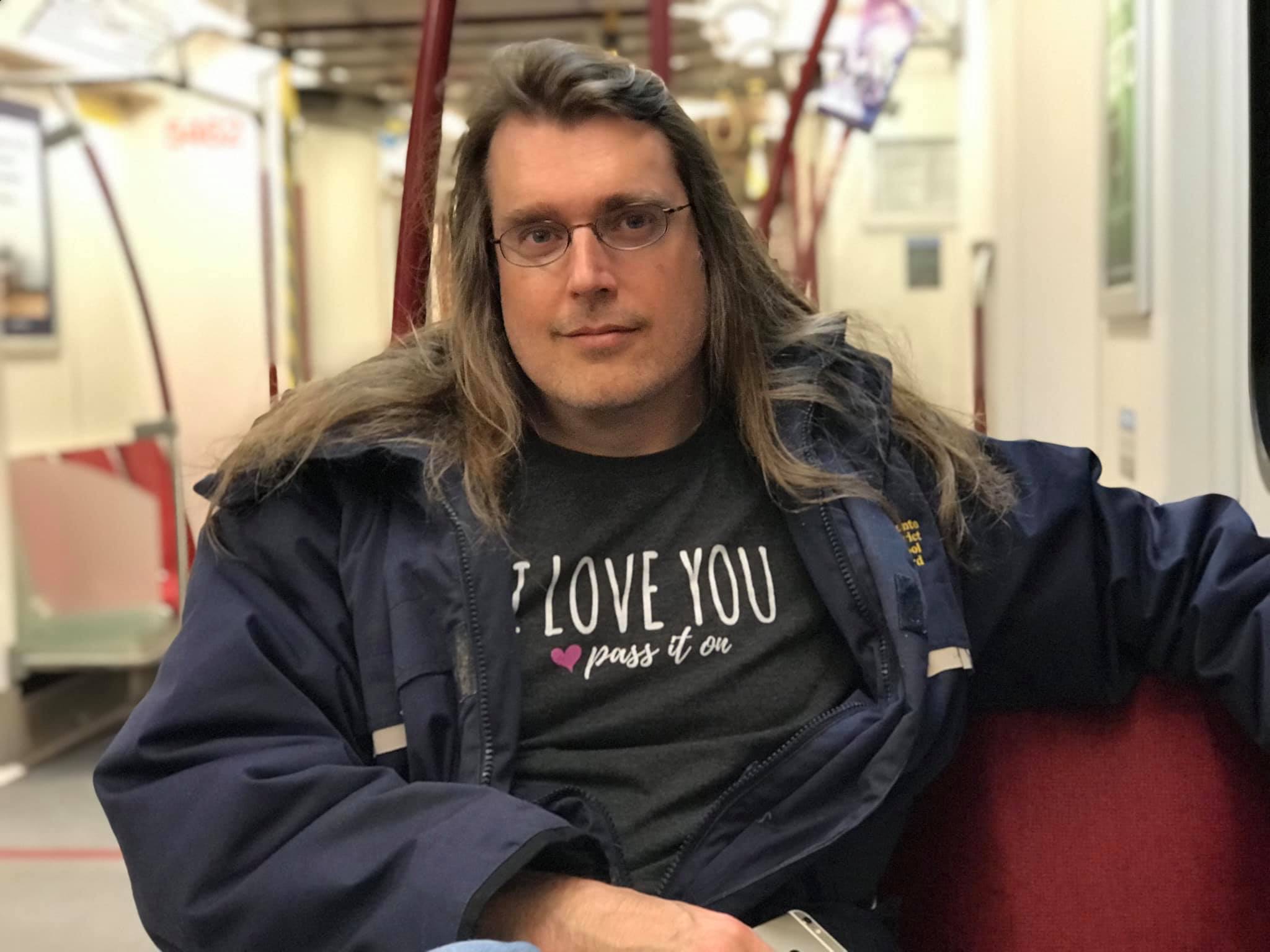 Shawn wearing an I Love You Pass It On shirt on the subway